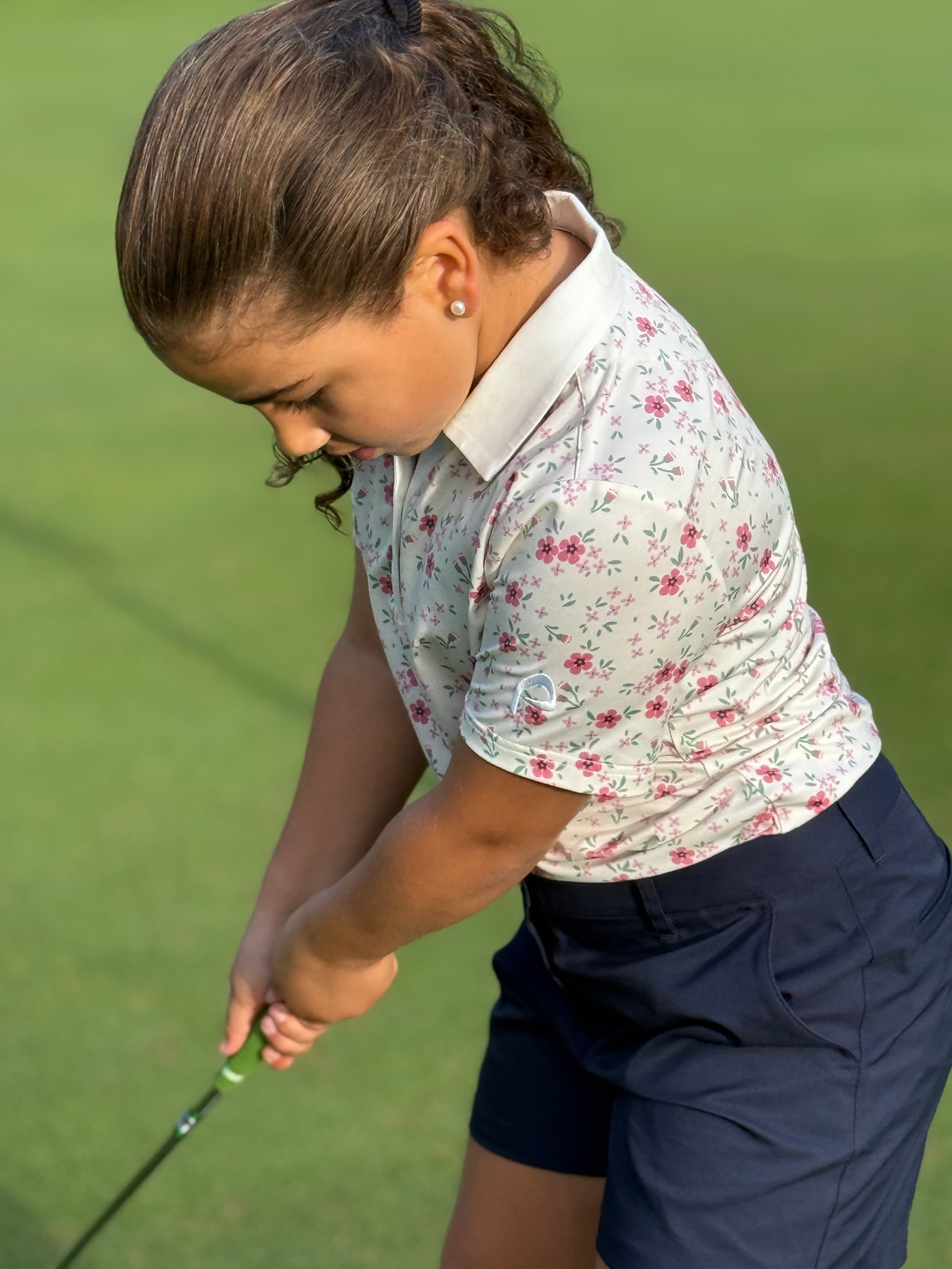 Young girl playing golf on a green course wearing Pitchn Blossom Polo Shirt